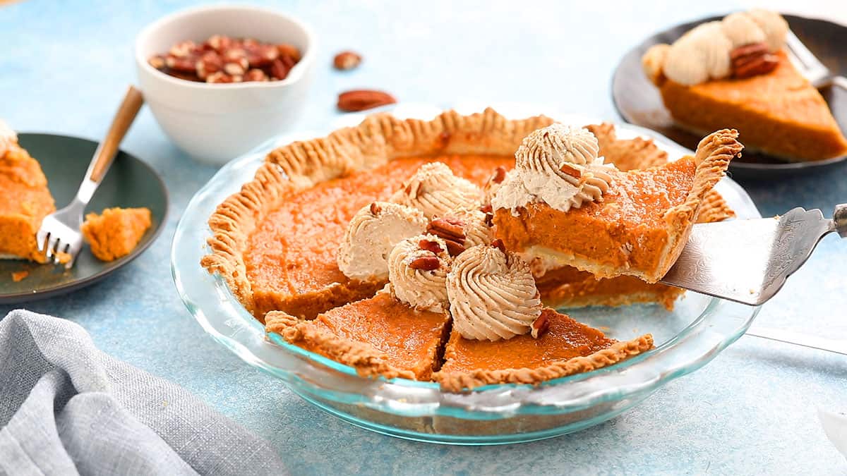 a hand lifting a slice of sweet potato pie from a glass pie dish.