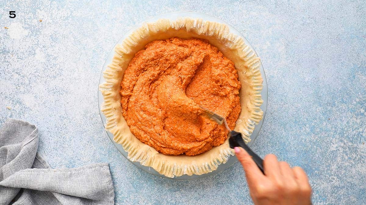 a hand swirling sweet potato filling in an unbaked pie crust in a glass dish.