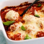 White cheese topped chicken meatballs in red sauce in a white baking dish.