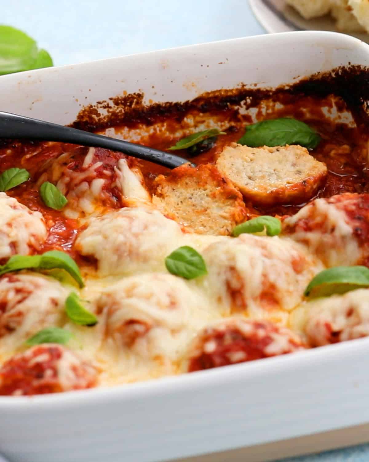 White cheese topped chicken meatballs in red sauce in a white baking dish.