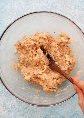 a hand mixing chicken meatball mixture in a glass bowl.