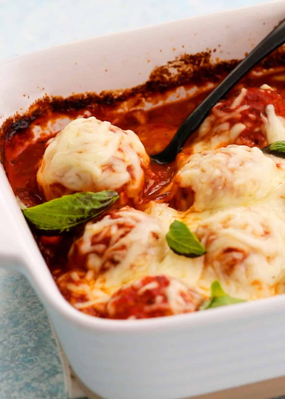 White cheese topped chicken meatballs in red sauce in a white baking dish.
