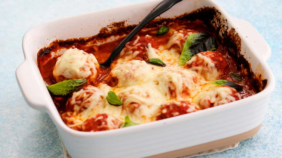 White cheese topped chicken meatballs in red sauce in a white baking dish.