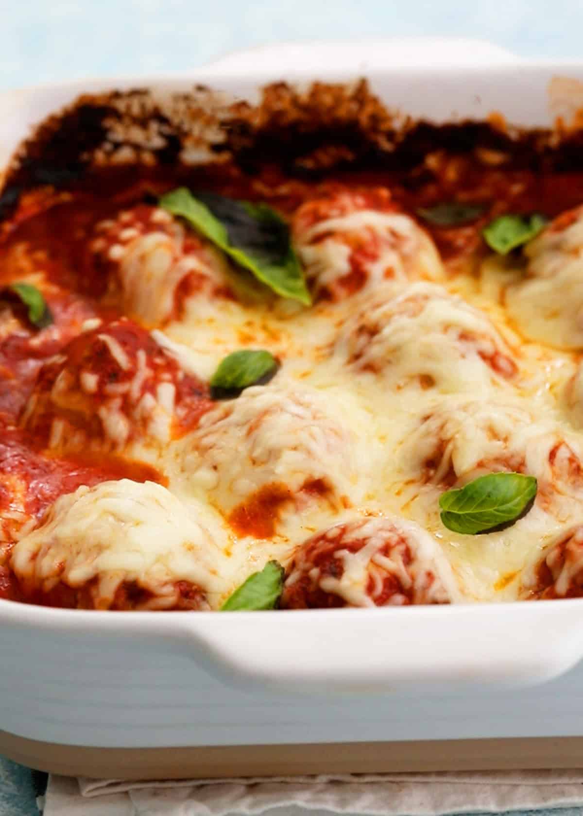 White cheese topped chicken meatballs in red sauce in a white baking dish.