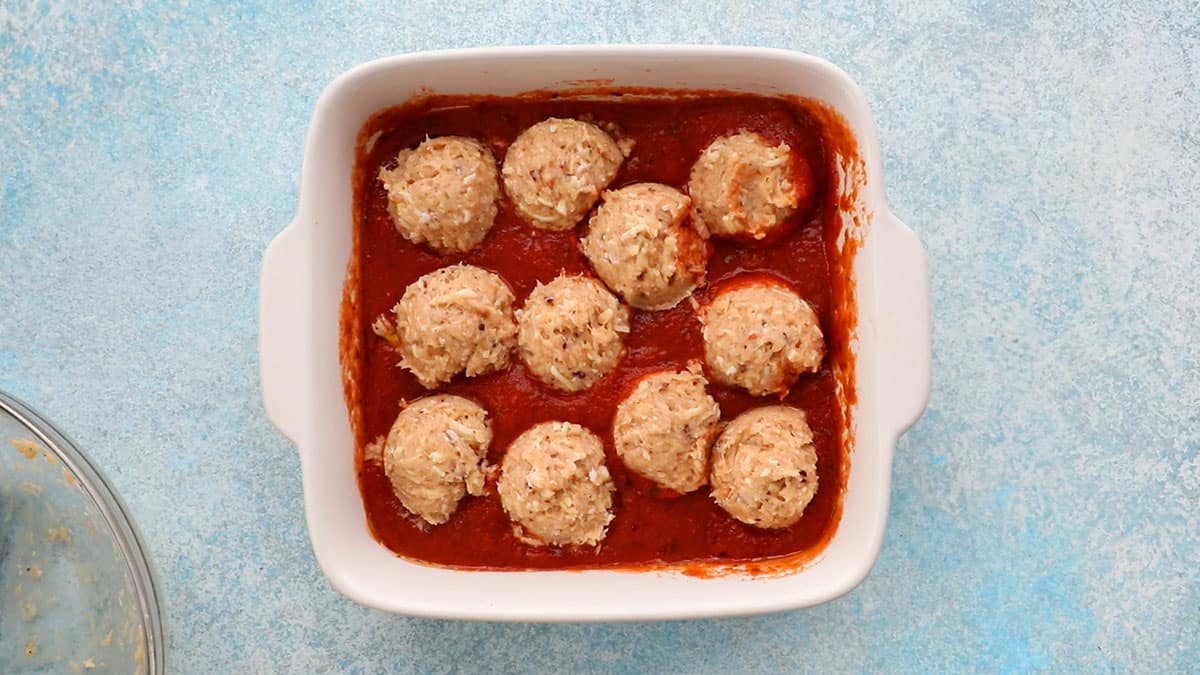 chicken meatballs in a white baking dish with red sauce.