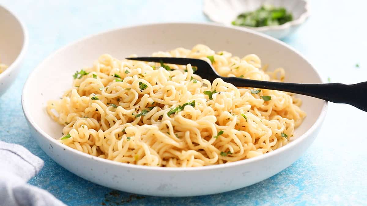 white buttered noodles in a round white plate along with a black fork.