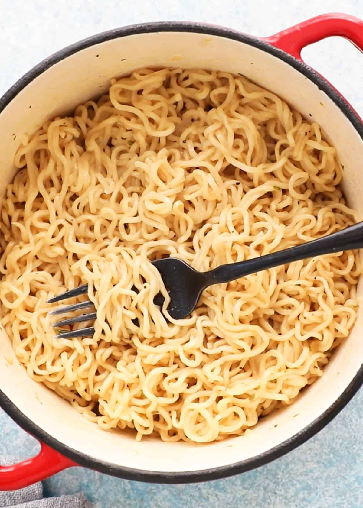 cooking ramen noodles in a white pot along with a black fork.