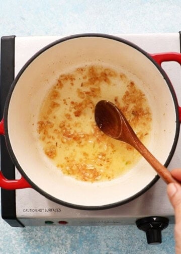 a hand cooking garlic in a white pot.