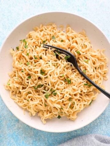 white buttered noodles in a round white plate along with a black fork.
