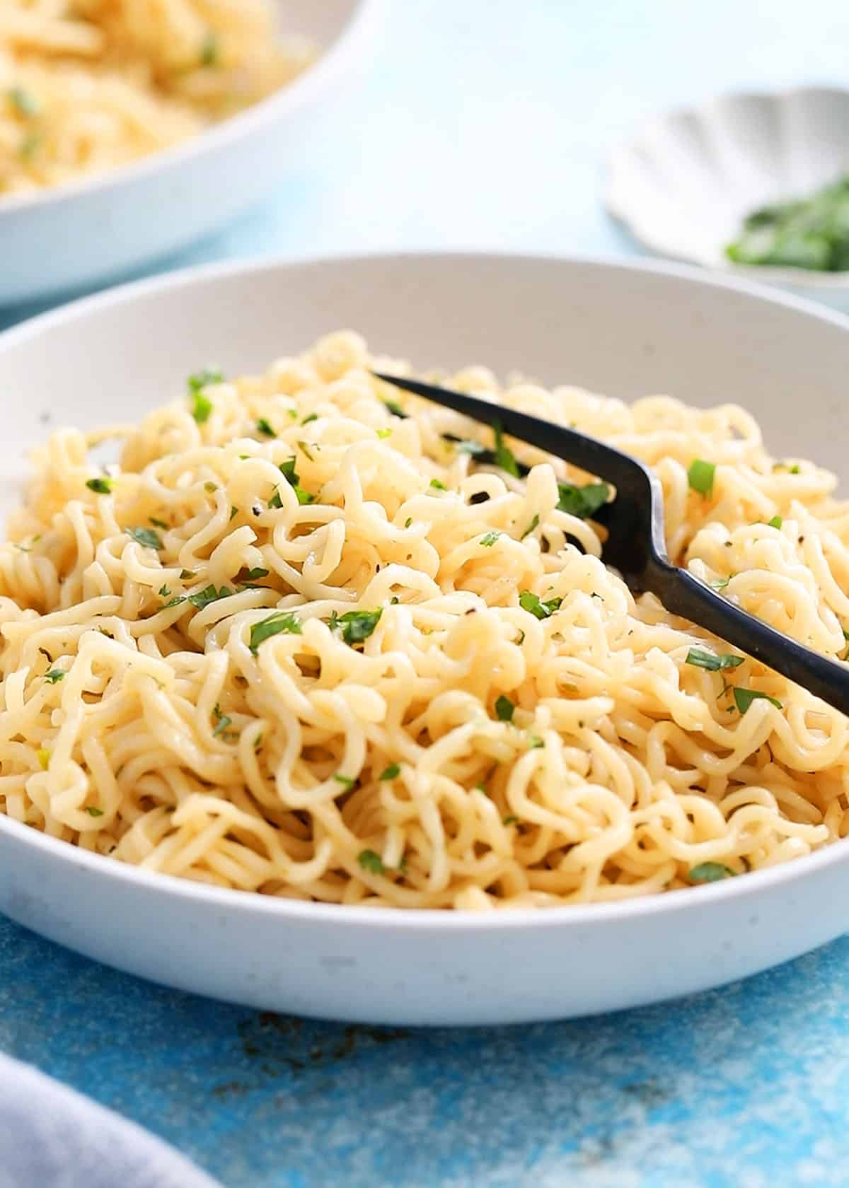 white buttered noodles in a round white plate along with a black fork.