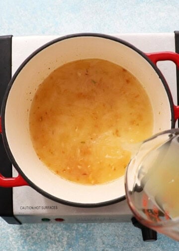 a hand pouring yellow stock into a white pot.