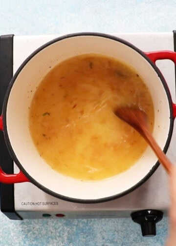 a hand stirring yellow stock in a white pot.
