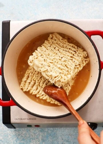 two squares of dried ramen noodles placed in yellow stock in a white pot.
