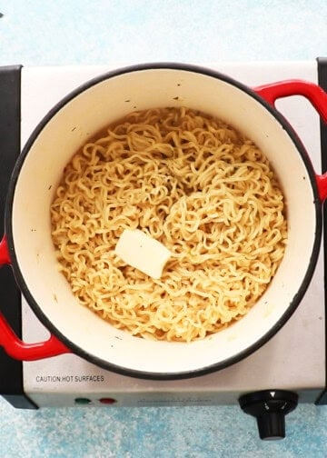 cooked yellow ramen noodles along with a piece of butter in a white pot.