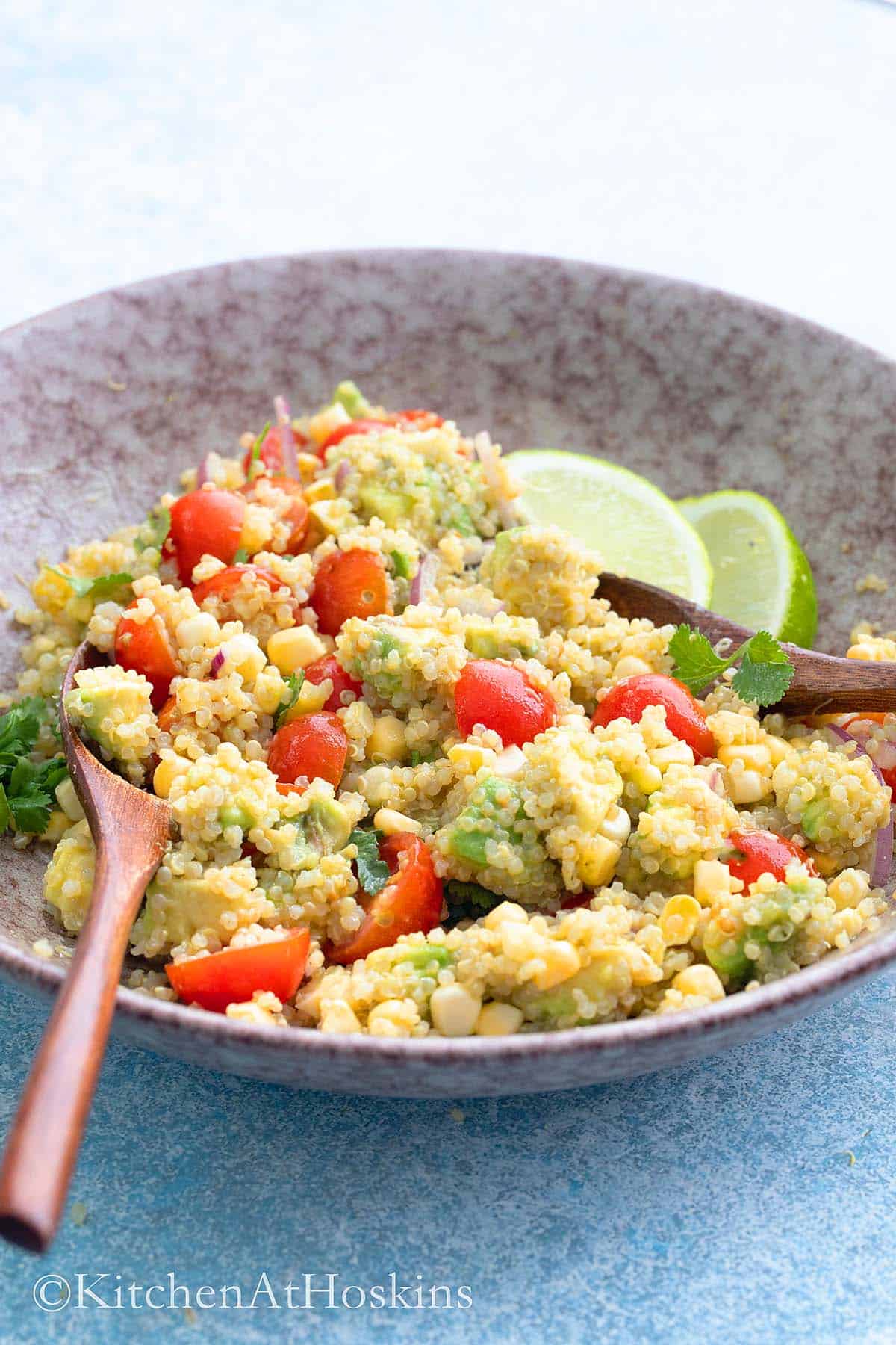 pink bowl with quinoa salad along with 2 wooden spoons.