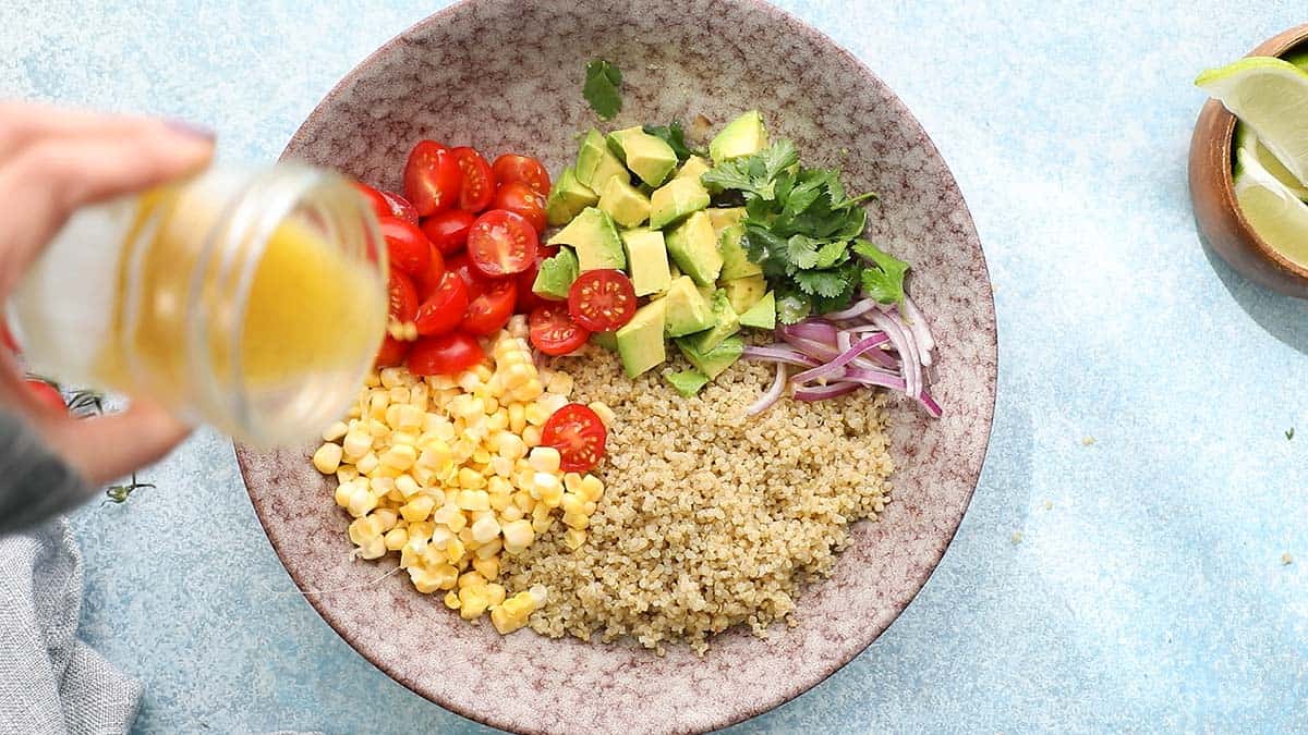 a hand pouring dressing from a glass jar over a pink bowl with salad ingredients. 