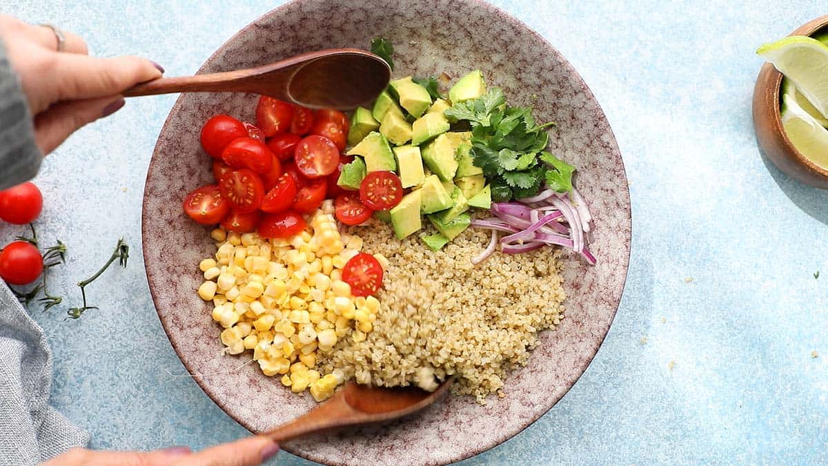 2 hands tossing salad in a pink bowl with 2 wooden spoons.