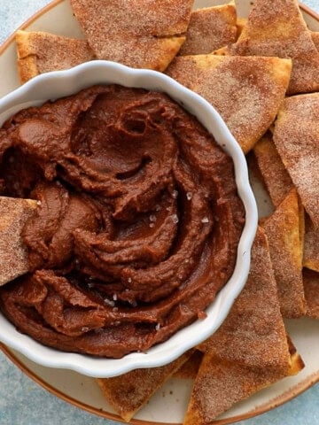 a hand dipping one triangle chip into brown hummus dip.