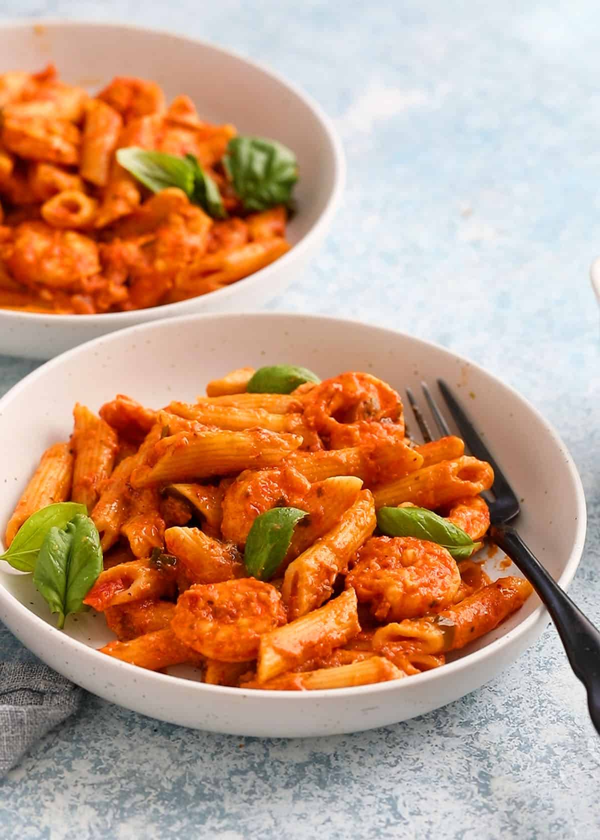 red shrimp pasta in two white bowls along with a black fork.