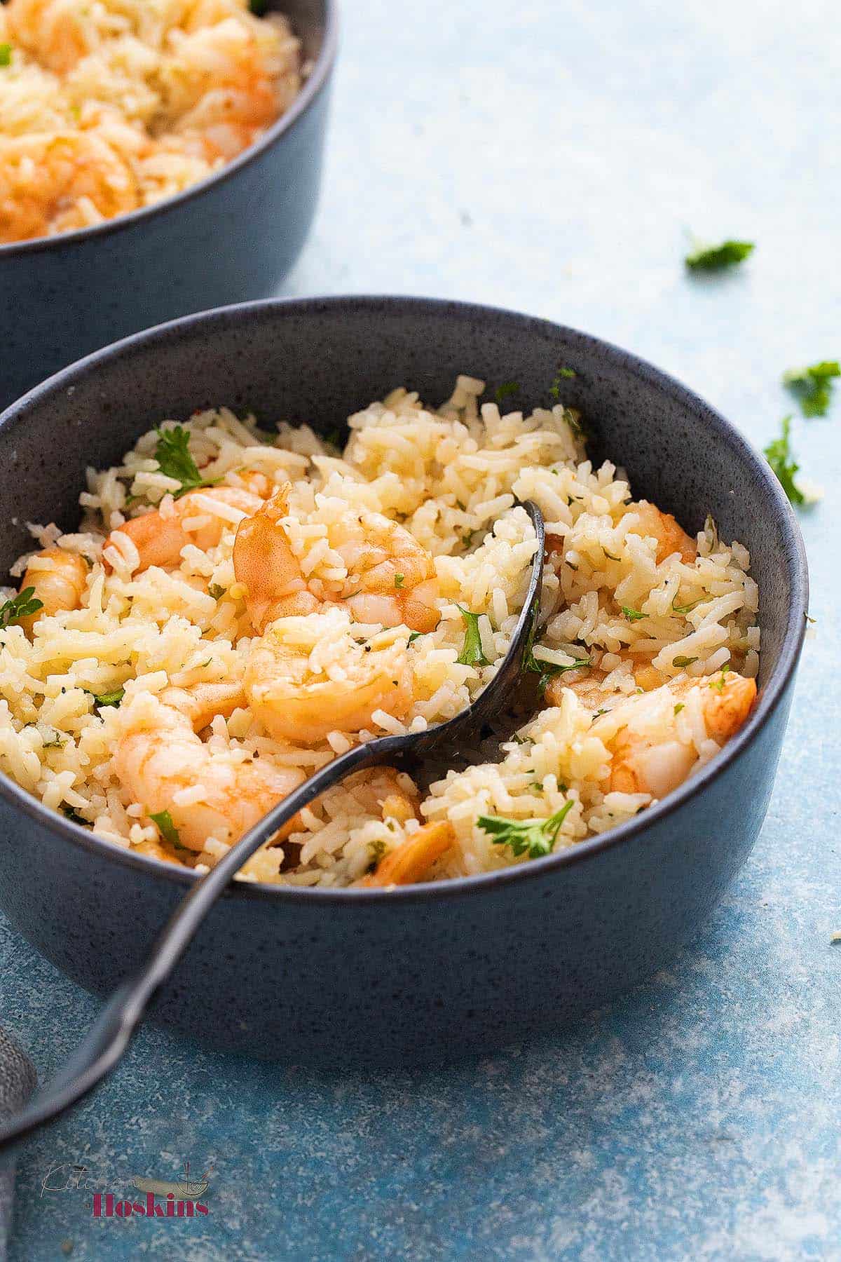 one blue bowl with cooked rice and shrimp along with a black spoon.