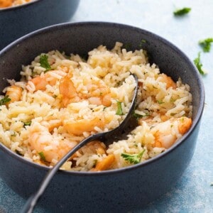 one blue bowl with cooked rice and shrimp along with a black spoon.