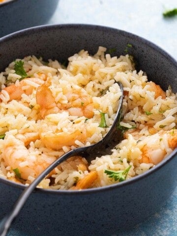 one blue bowl with cooked rice and shrimp along with a black spoon.