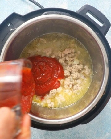 a hand pouring red sauce into an instant pot.