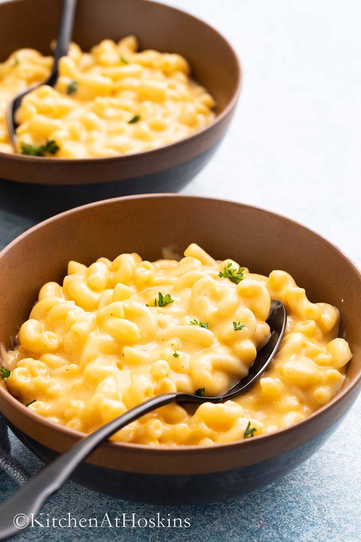 2 brown bowls with macaroni and cheese with black spoon.