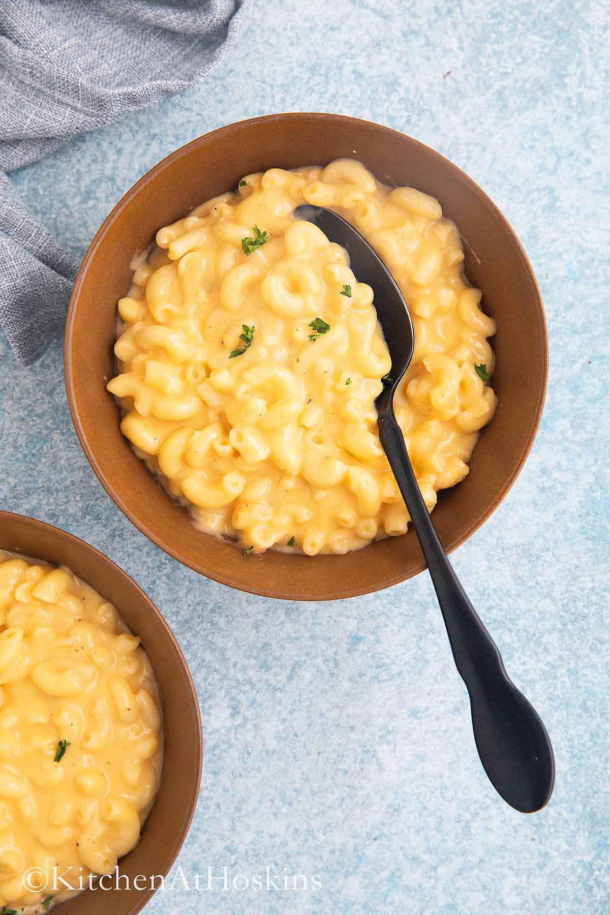 2 brown bowls with cooked mac and cheese and black spoon.