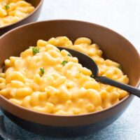 2 brown bowls with cooked macaroni and cheese with black spoons.