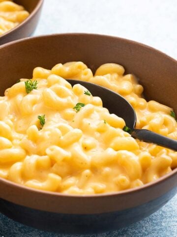 2 brown bowls with cooked macaroni and cheese with black spoons.