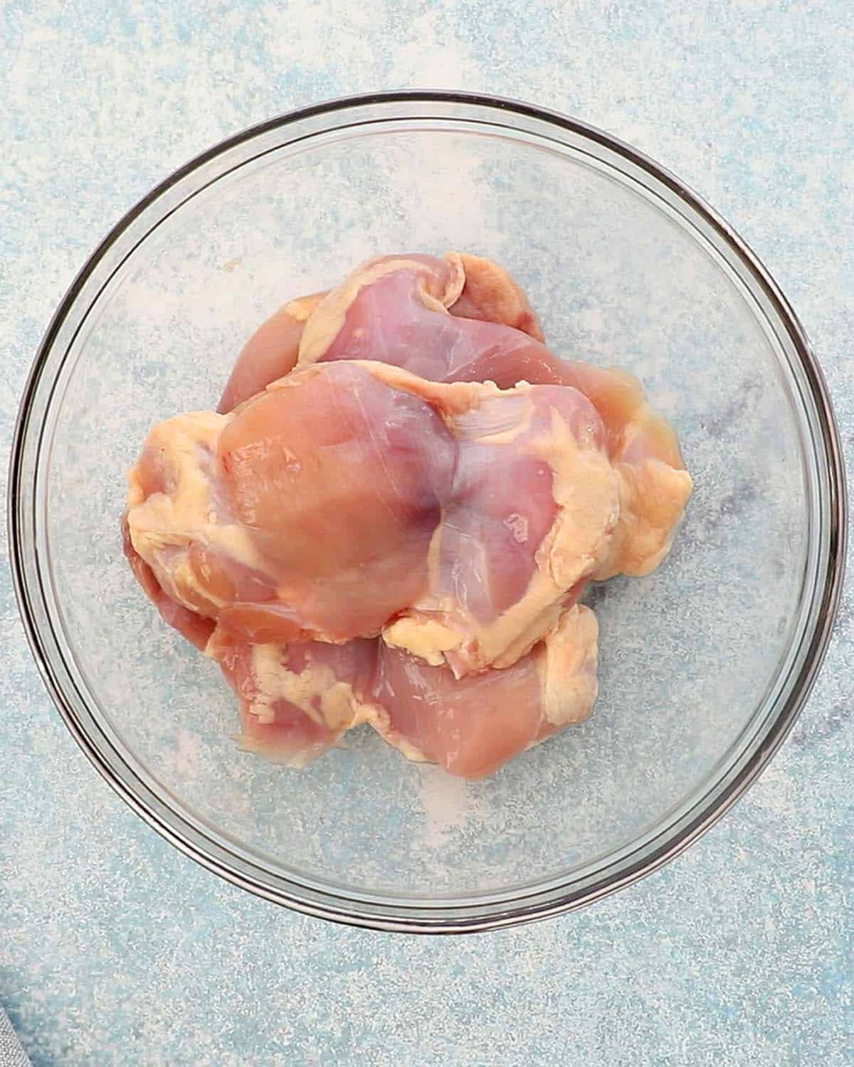 4 raw boneless chicken thighs in a glass bowl.
