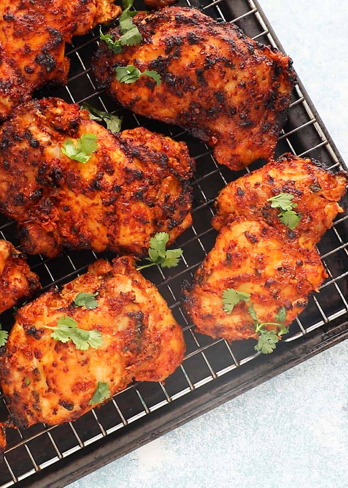 5 cooked red colored tandoori chicken thighs placed on a wire rack.