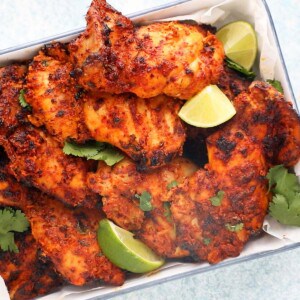 cooked tandoori chicken thighs placed in a white tray along with lime wedges.
