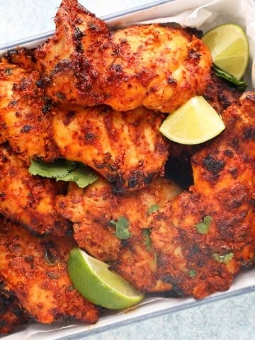 cooked tandoori chicken thighs placed in a white tray along with lime wedges.