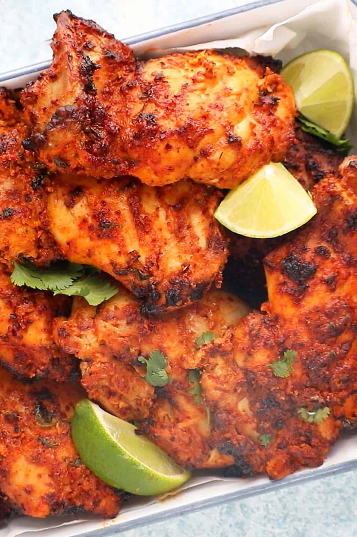 orange colored tandoori chicken thighs in a white platter.