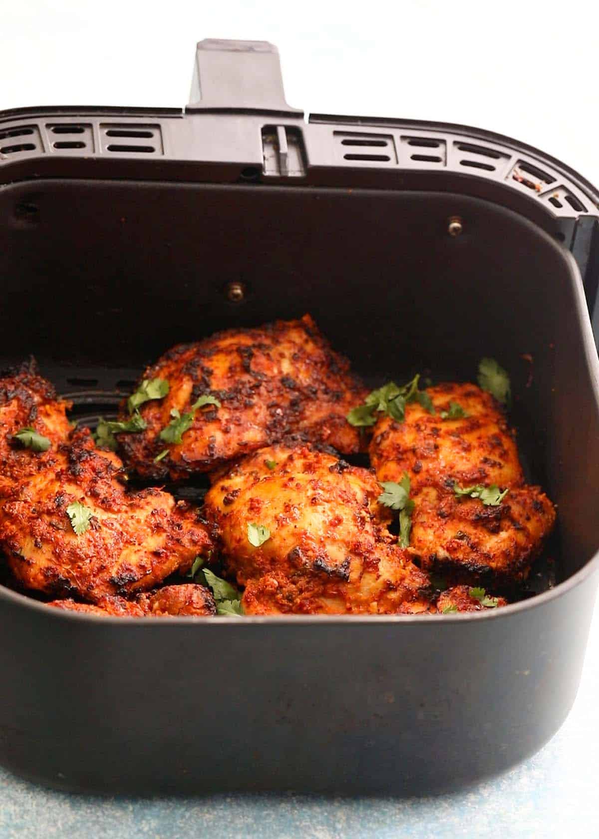 cooked tandoori chicken thighs in an air fryer basket.