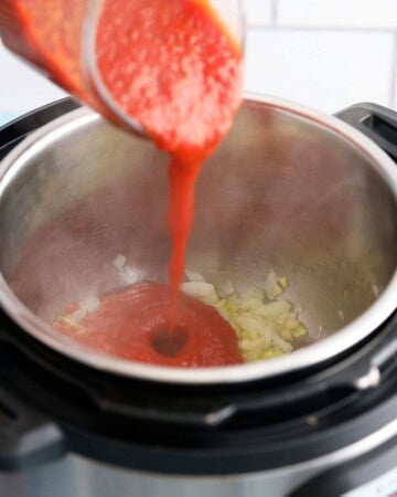 a hand pouring red sauce into an instant pot.