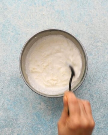 a hand mixing white sauce in a blue bowl.