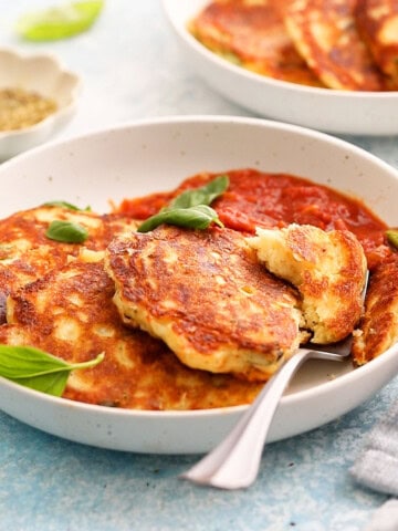 3 cooked savory pancakes along with red sauce placed in a white plate.