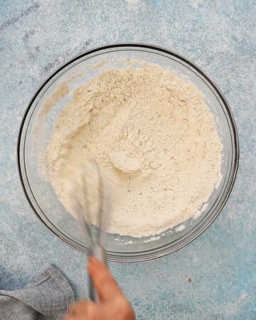 a hand whisking white flour in a glass bowl.