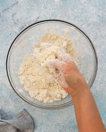 a hand mixing white flour in a glass bowl.