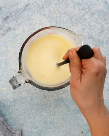 a hand mixing yellow milk in a glass measuring cup.