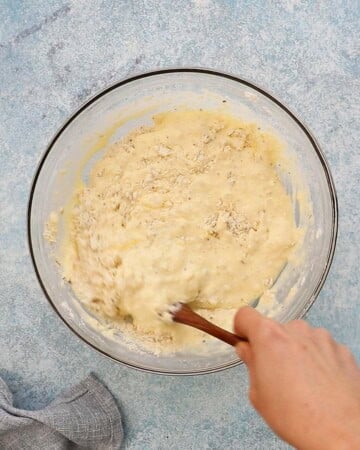 a hand mixing pancake batter in a glass bowl.