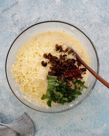 pancake batter with cheese and olives in a glass bowl.