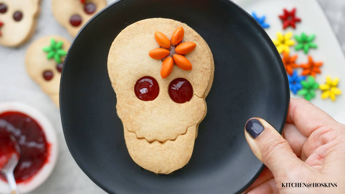 A hand holding a small black plate which has one decorated linzer cookie for Halloween