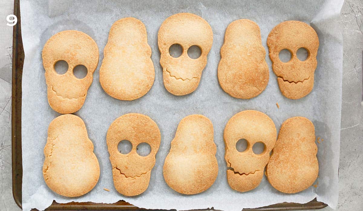 10 baked skull shaped cookies on a parchment lined baking sheet.