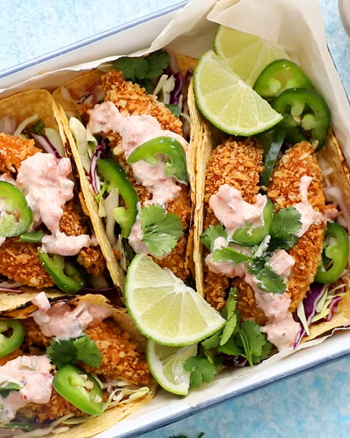 4 assembled fish tacos in a white tray.