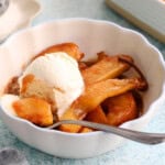 brown pear slices along with one white scoop of ice cream in a white bowl.