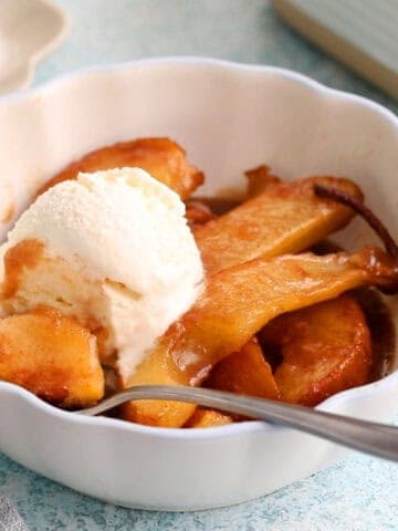 brown pear slices along with one white scoop of ice cream in a white bowl.